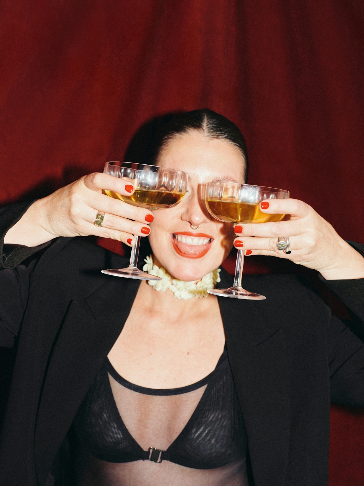 Woman raising two coupe glasses in a toast in front of a red curtain